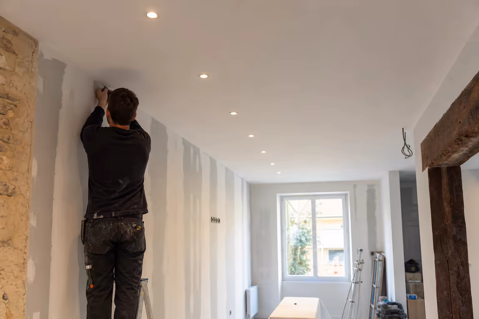 Faux plafond fraîchement posé dans un salon d&#39;échoppe bordelaise rénovée, spots LED encastrés alignés au cordeau, finition blanc mat prête à peindre, lumière naturelle entrant par une grande fenêtre
